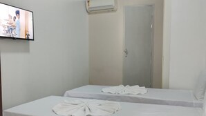 A single-bed room with a tiled floor, a white bedspread, a flat-screen TV mounted on the wall, and a door with a mirror. - Pousada Belo Mar (Salvador)