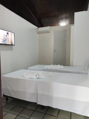 A single-bed room with a tiled floor, a white bedspread, a flat-screen TV mounted on the wall, and a door with a mirror. - Pousada Belo Mar (Salvador)