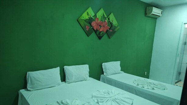 A room with two beds, each with white bedding and a towel on the bed. There is a green wall and a painting of flowers above the beds. - Pousada Belo Mar (Salvador)