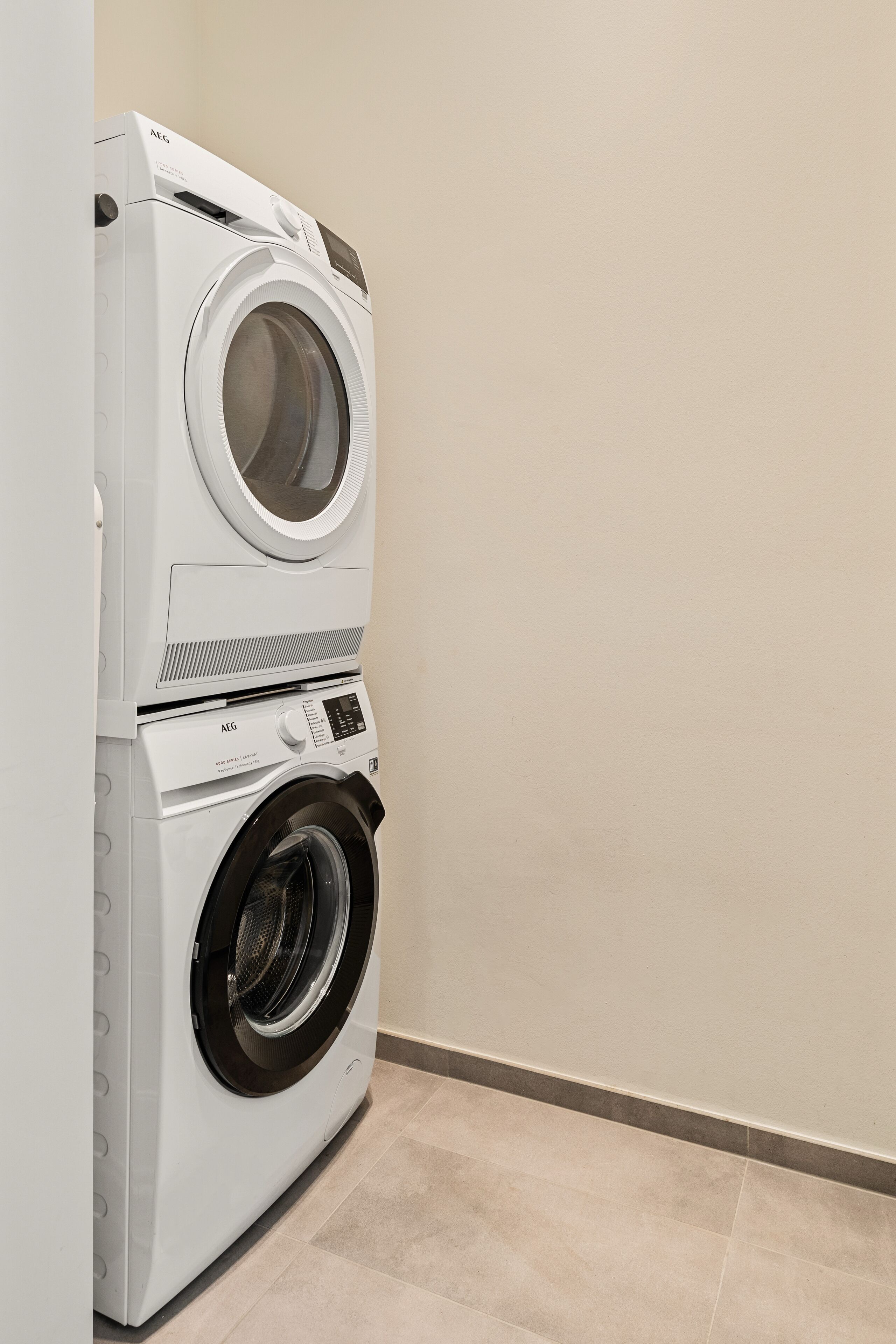 A stacked washer and dryer unit in a corner with a plain wall and tiled floor.