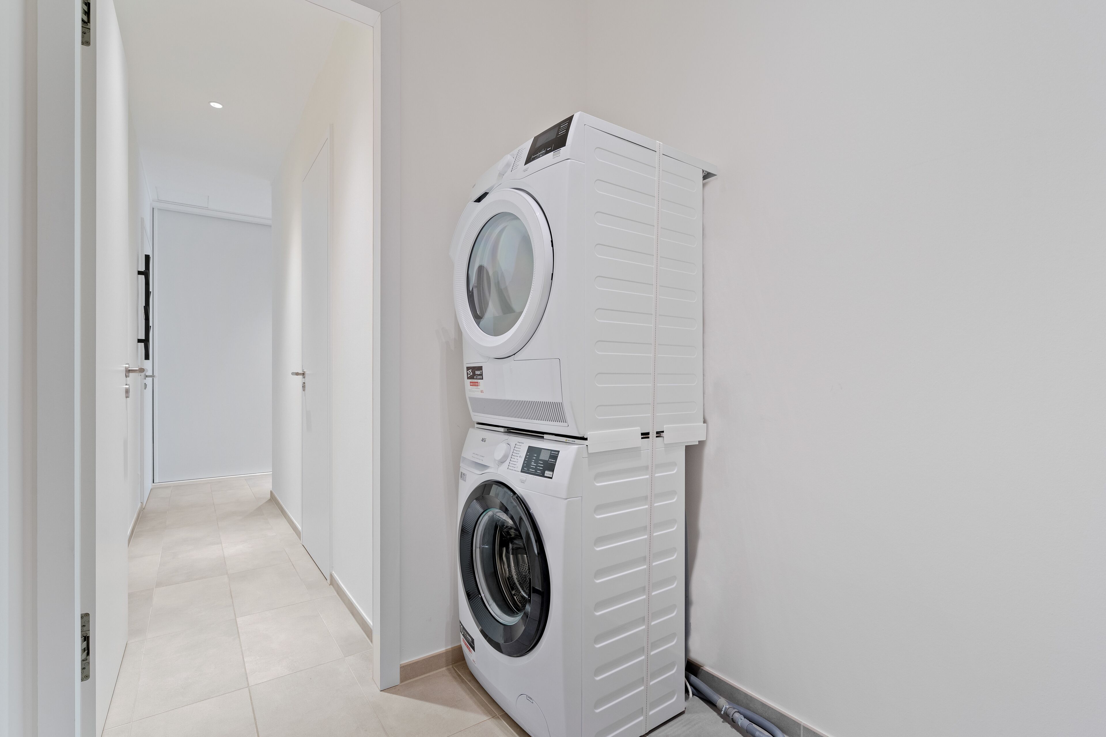 A laundry room with stacked washing machines and dryers, a tiled floor, and a white door in the background.