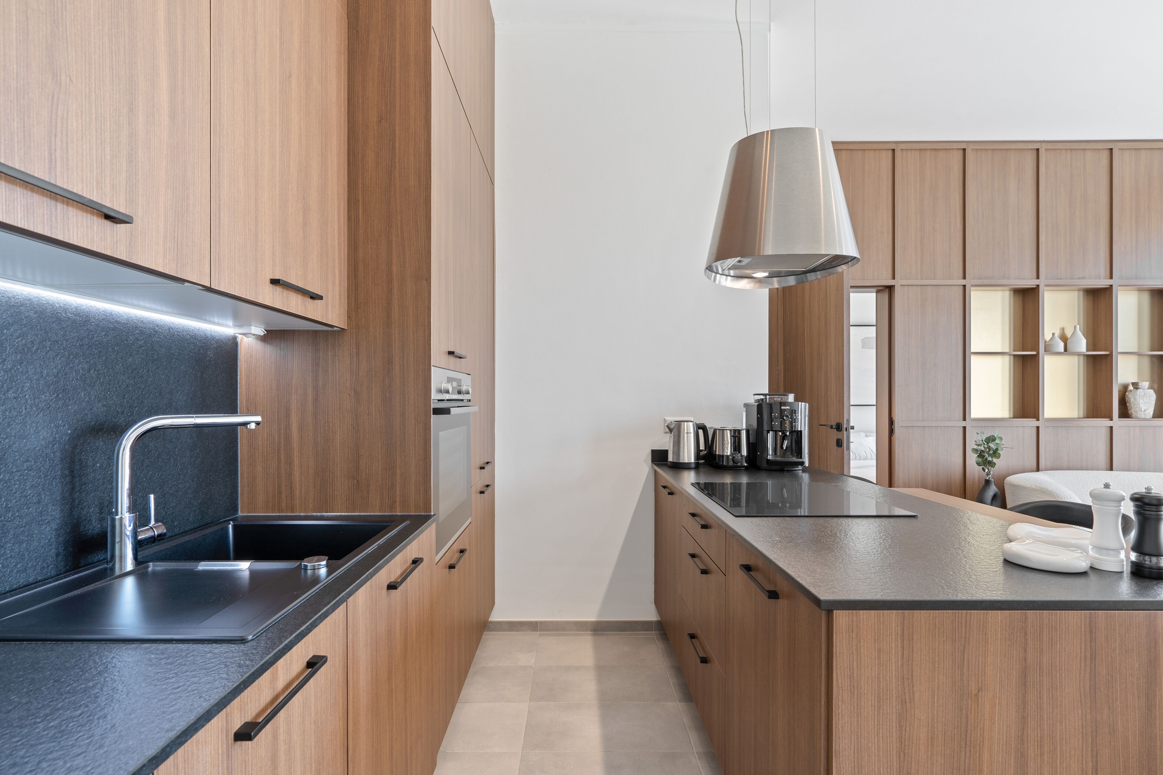 Une cuisine moderne avec des meubles en bois, un plan de travail noir et un luminaire suspendu.