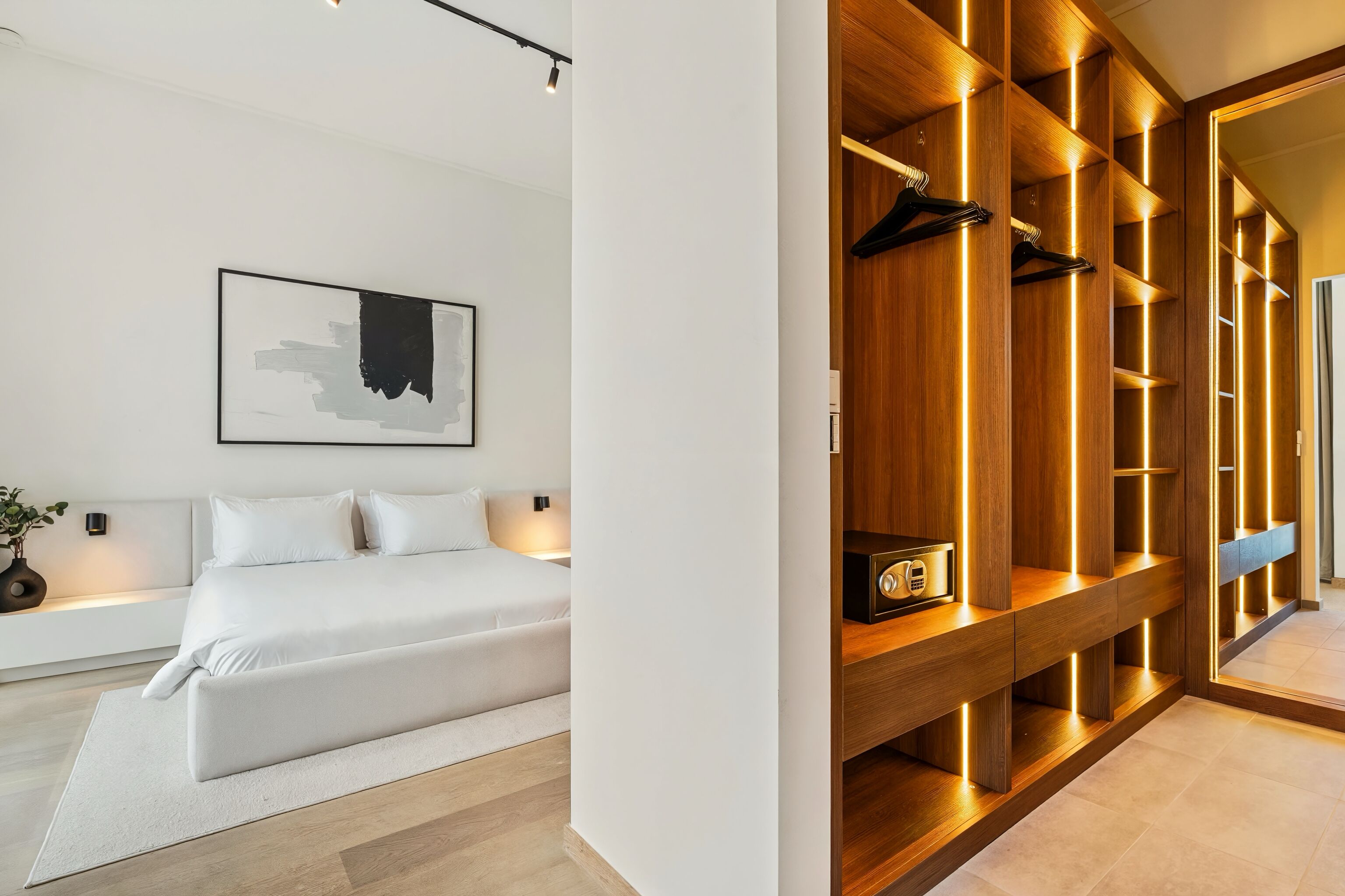 Un dormitorio moderno con una cama grande, una mesita de noche, un cuadro abstracto colgado en la pared y un armario de madera con iluminación integrada.