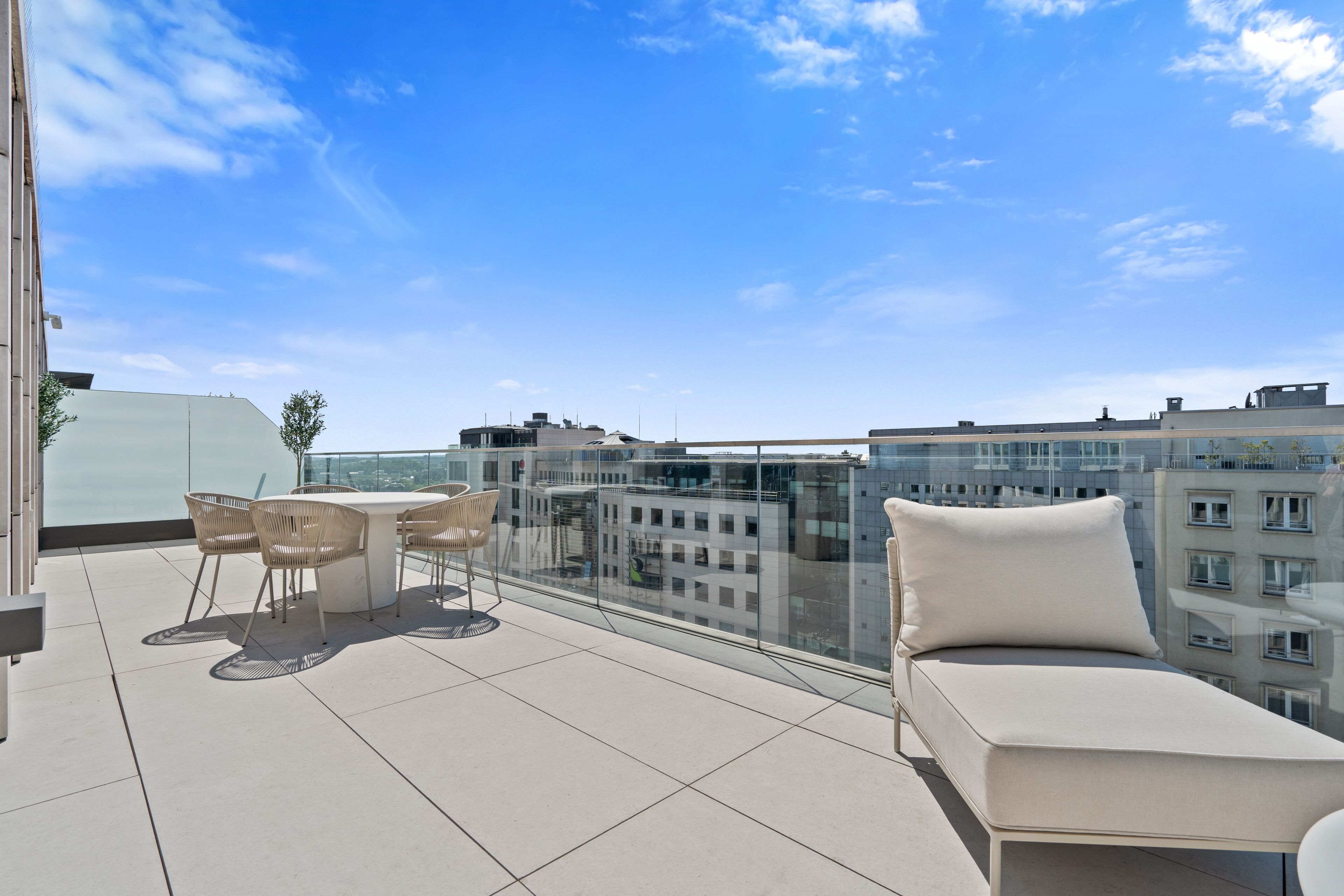 A rooftop terrace with a glass balustrade, a white sofa, and wicker chairs.