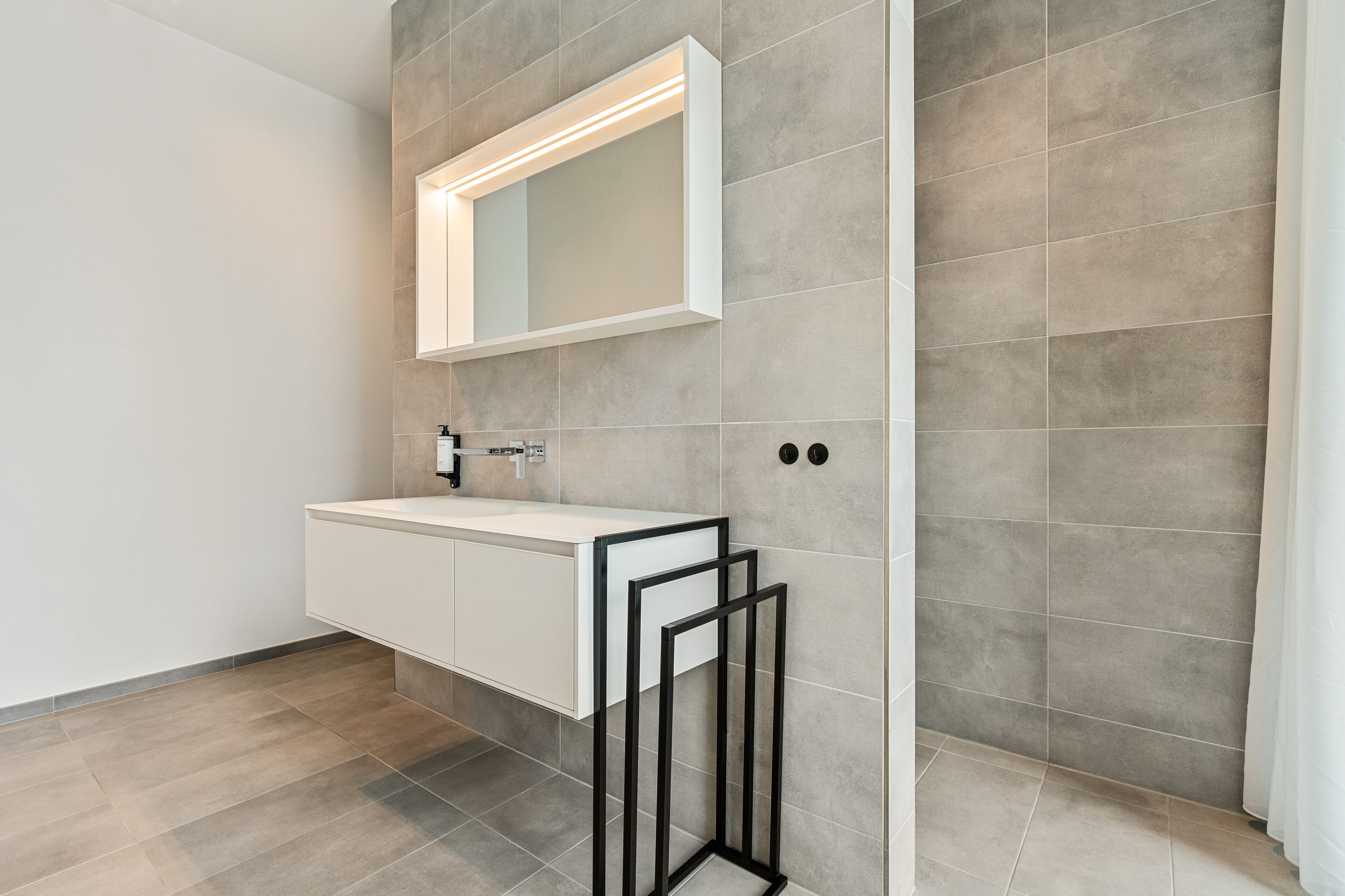 A modern bathroom with a white vanity, a mirror with integrated lighting, and a tiled floor.