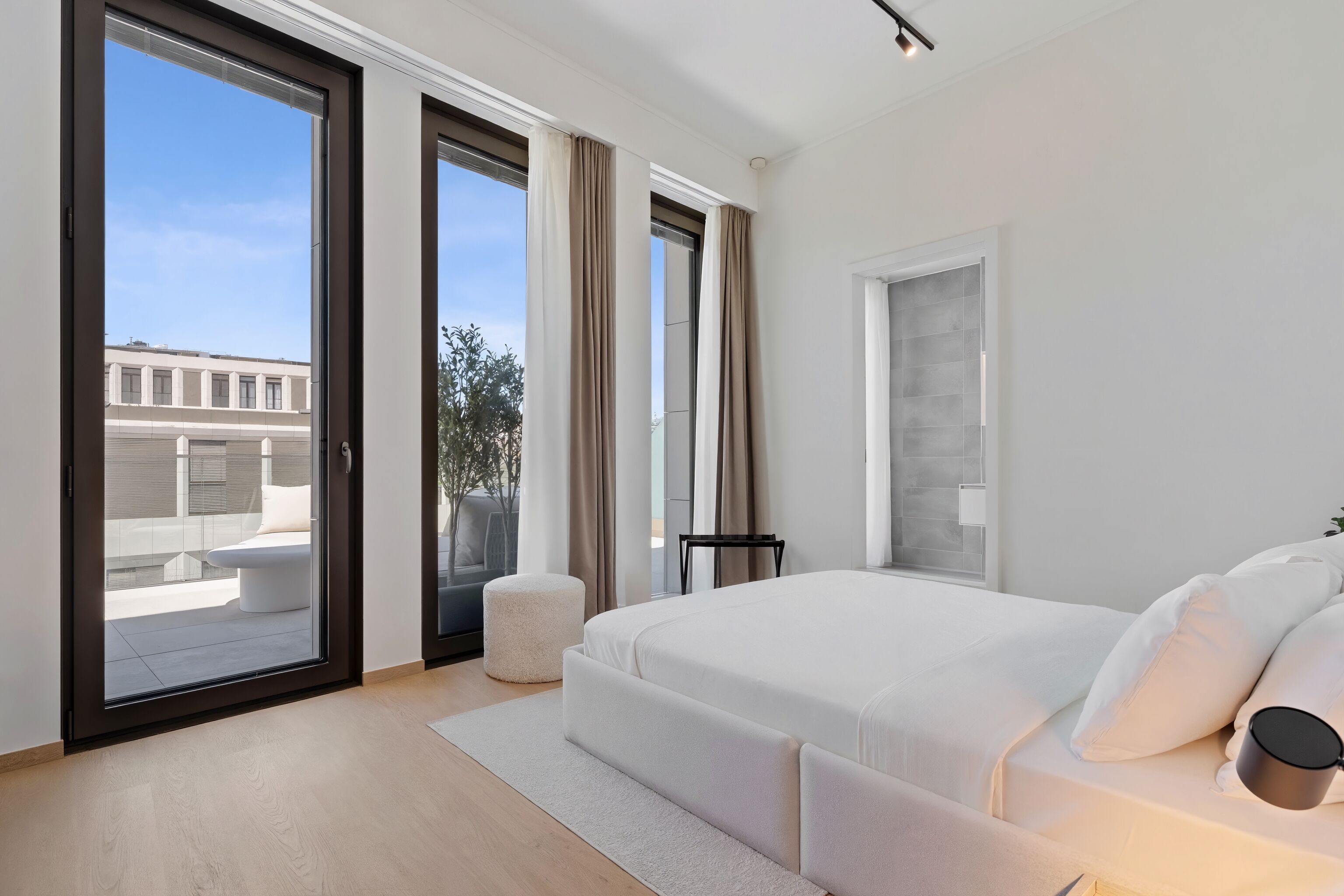 Un dormitorio moderno con una cama grande, puertas corredizas de vidrio a un balcón y vistas de edificios.