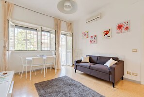 A modern living room with a sofa, a dining table with chairs, and a large window with curtains.