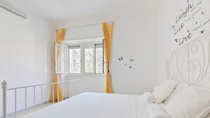 Un dormitorio con una cama, cortinas blancas, una ventana y una pared con citas motivacionales.