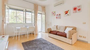 Un salón luminoso con sofá, una mesa de comedor con sillas y un ventanal con cortinas.