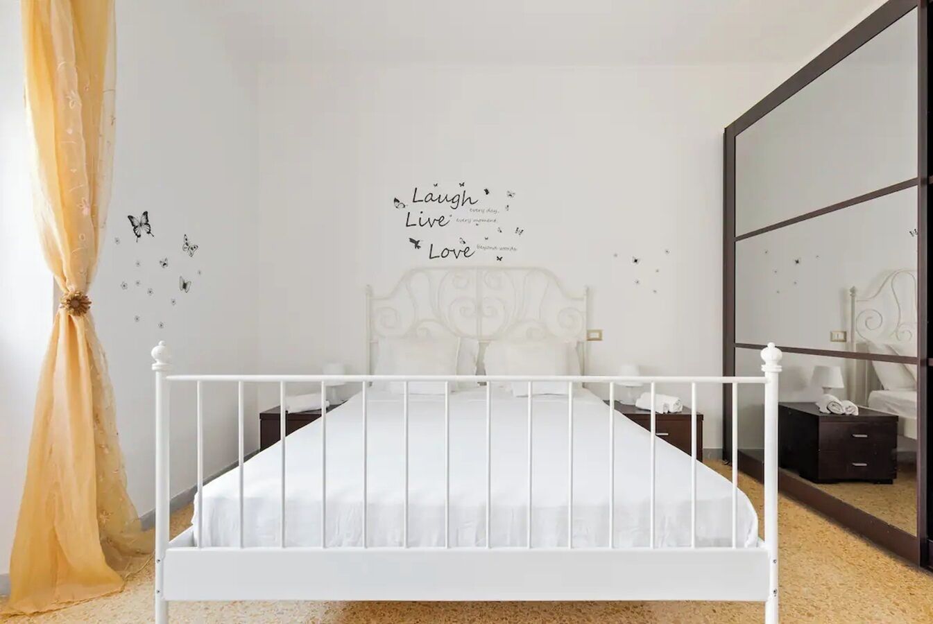 A bedroom with a white bed, a mirror, and wall decals with motivational phrases.