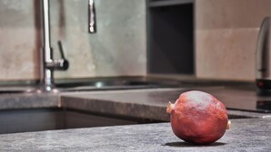 A pomegranate on a kitchen counter with a sink and faucet in the background.