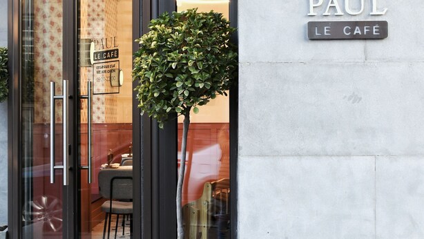 A cafe entrance with a glass door, a potted plant, and a sign reading "PAUL LE CAFE".