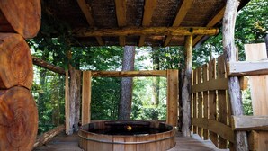 Een houten terras met een rond hottubbad, omgeven door houten leuningen en een bosrijke achtergrond.