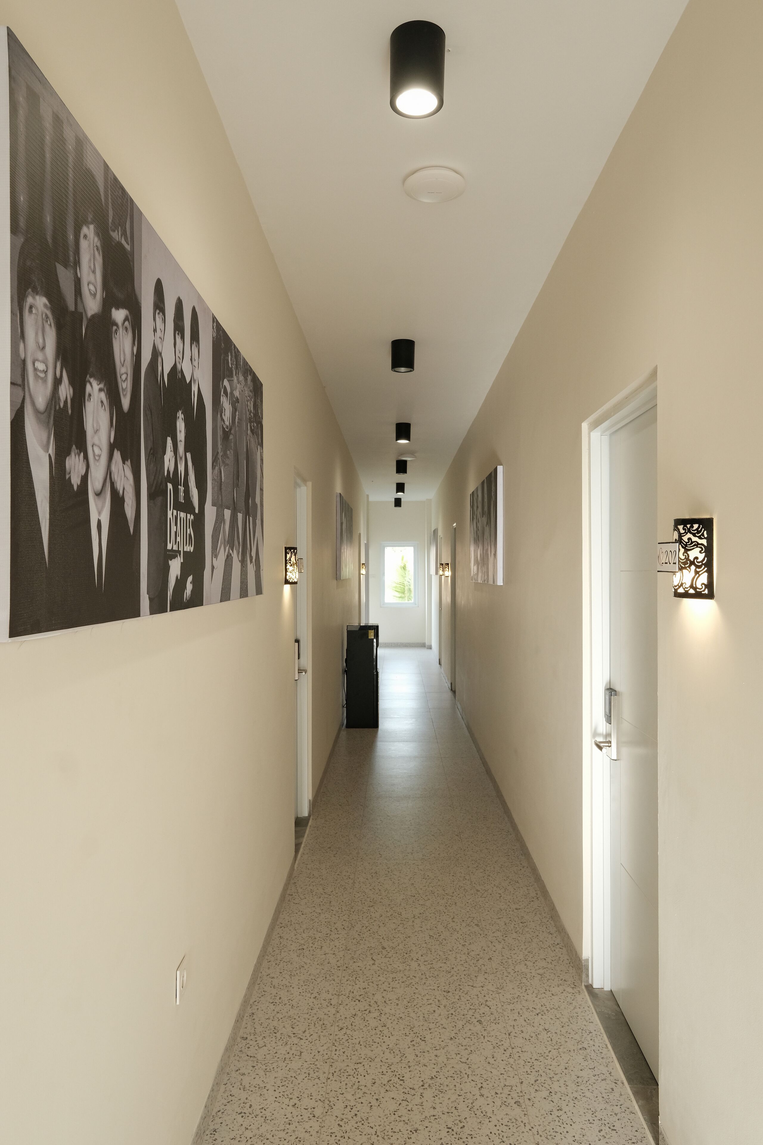 A hallway with a series of framed pictures on the walls, a light fixture on the ceiling, and a door on the right.