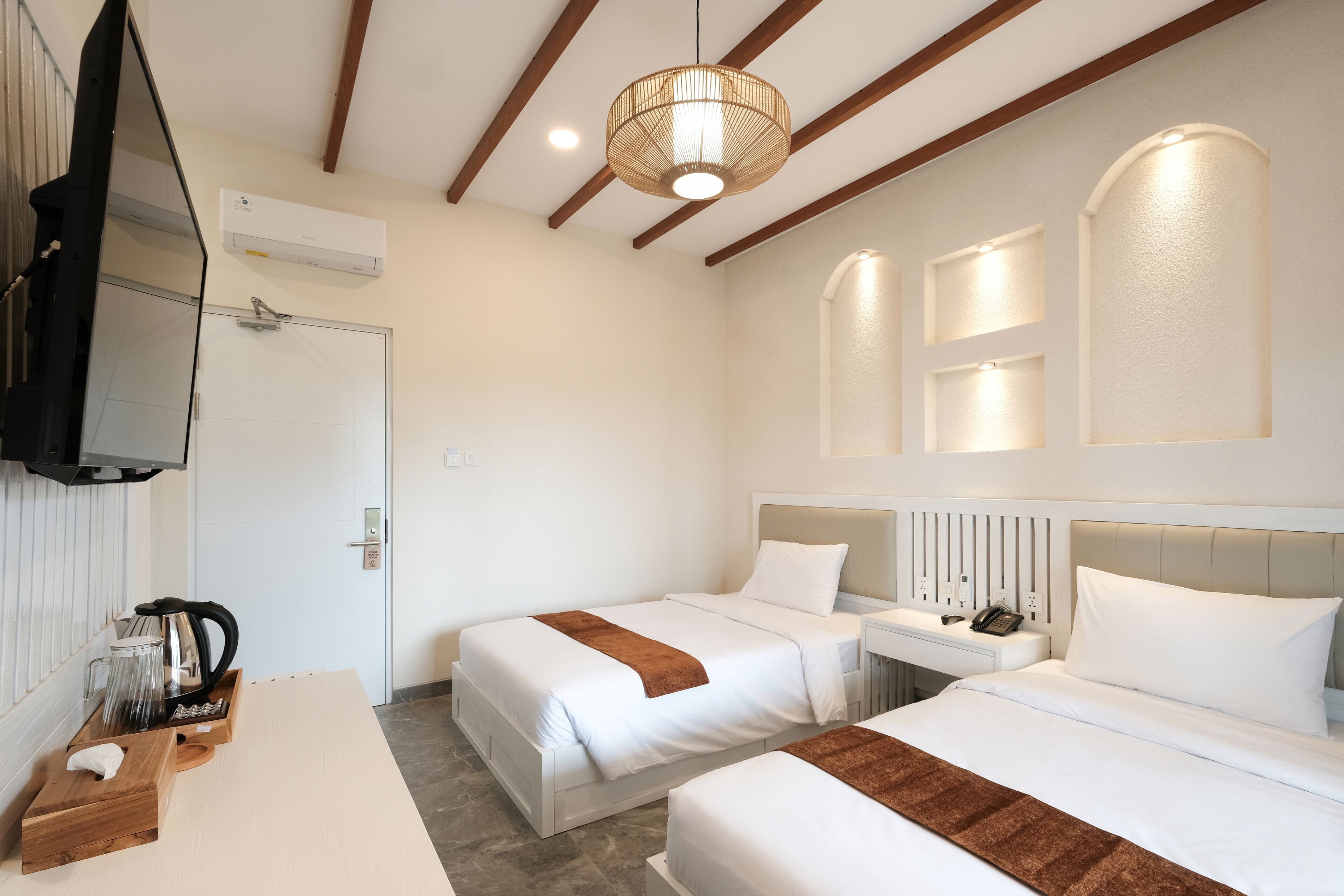 A hotel room with two beds, a bedside table, a TV, and a coffee maker.