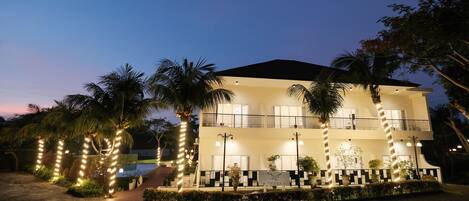 A two-story hotel with a balcony on the second floor, surrounded by palm trees and decorative lights.