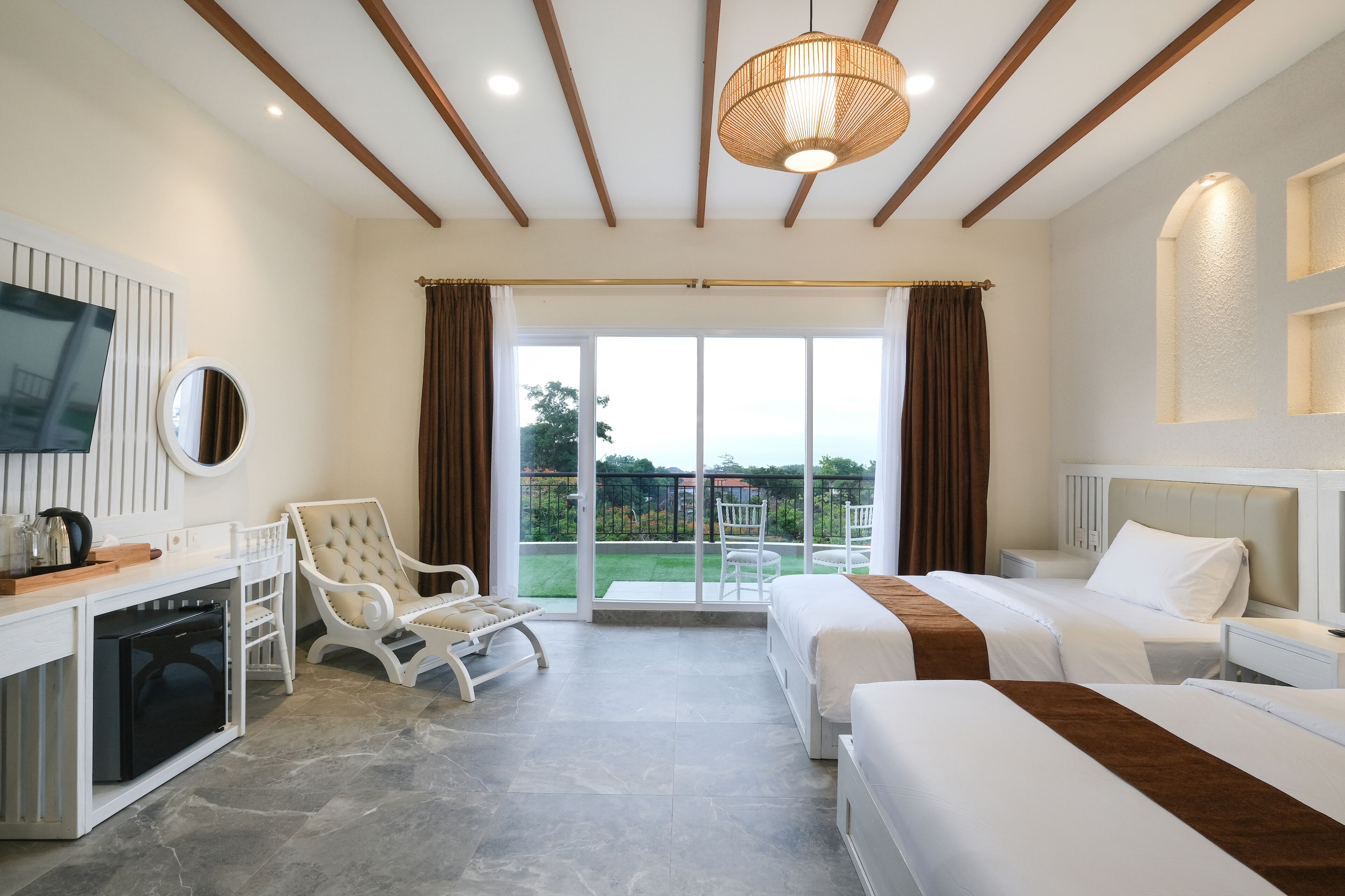 A hotel room with two beds, a desk with a television, a chair, and a view of the outdoors.