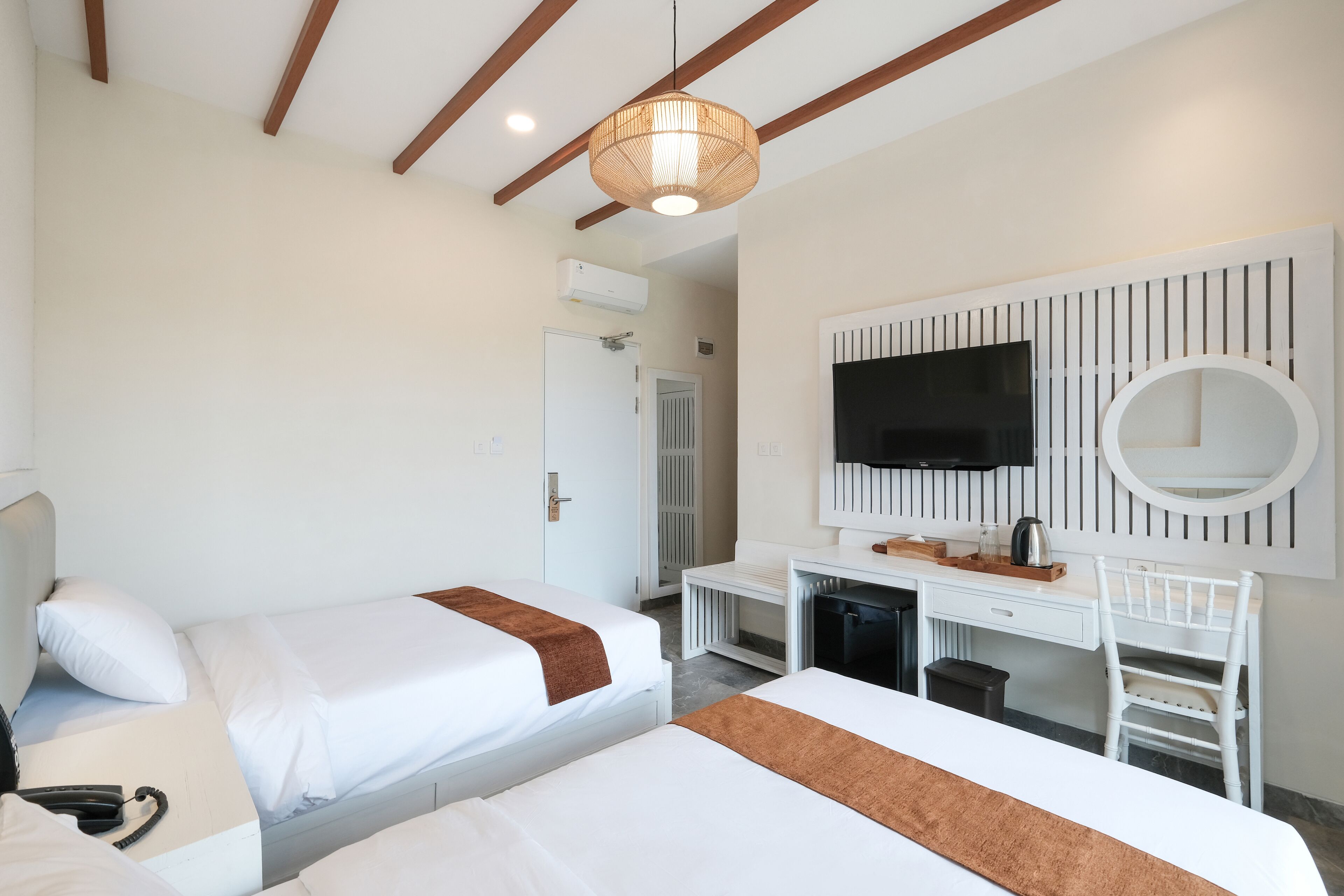 A hotel room with two beds, a desk, a chair, a TV, and a large mirror.