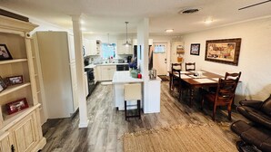 A compact kitchen with white cabinets, a dining area with a wooden table and chairs, and a living room with a brown leather couch.
