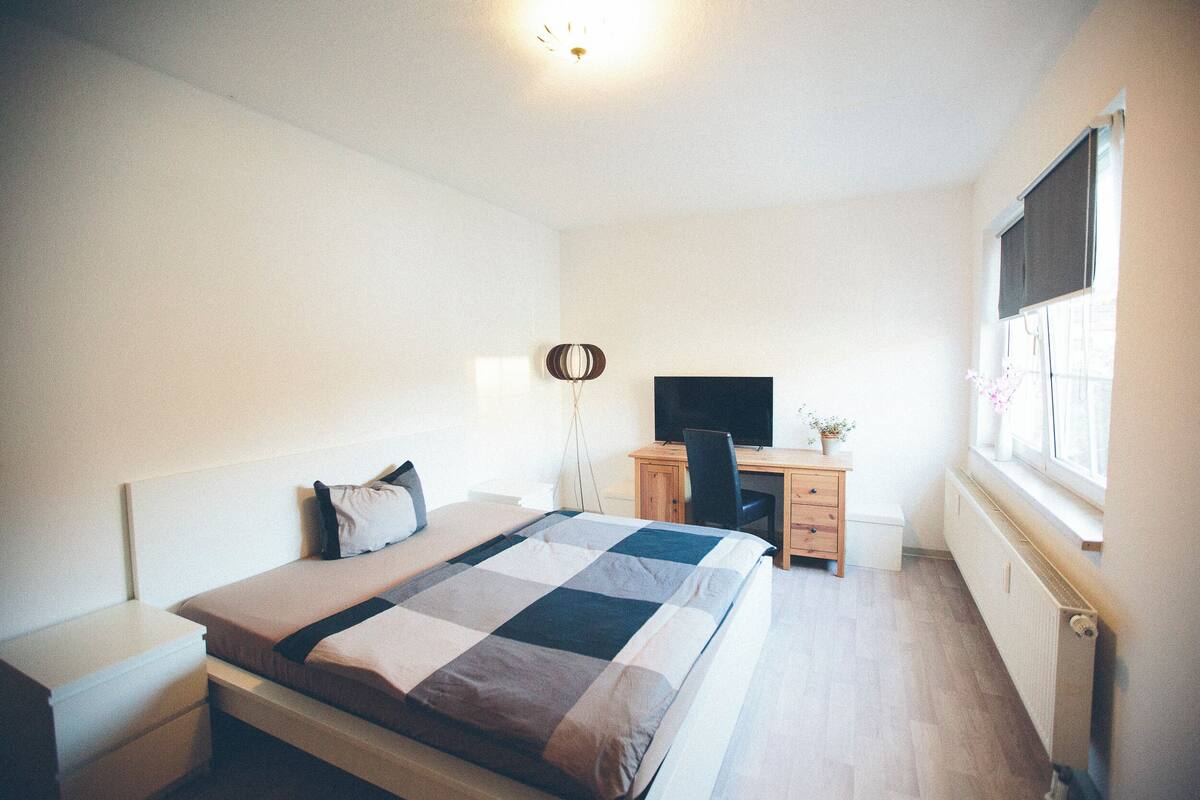 A bedroom with a bed, a desk, a chair, and a television.