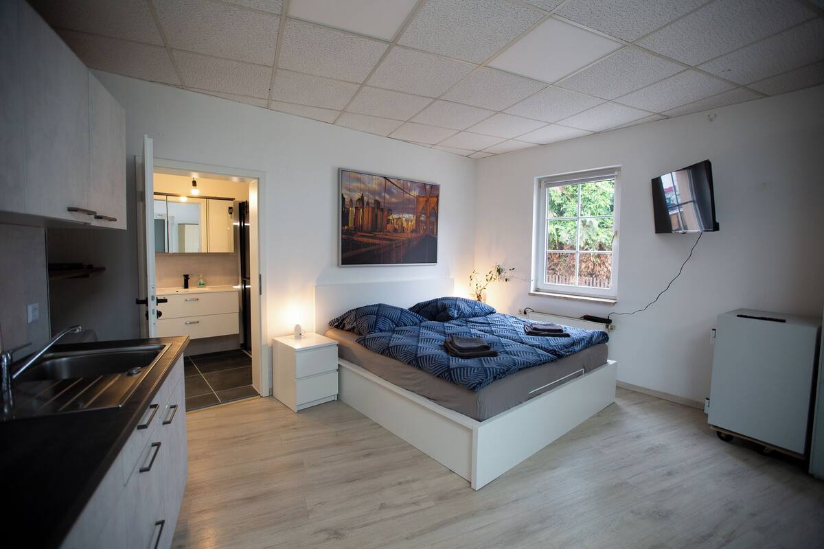 A modern bedroom with a bed, bedside tables, a TV, and a window.