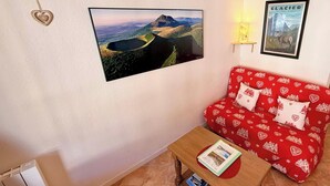 Una sala de estar con un sofá rojo, un cuadro de un paisaje montañoso, una decoración con forma de corazón y un cartel enmarcado en la pared.