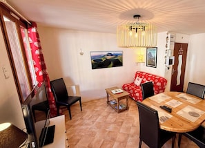 A living room with a red sofa, a wooden dining table, a TV, and a chandelier. - La Rivière 103 Le Mont Dore (Mont-Dore)