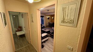 Un pasillo con un banco de madera, una zona de comedor con una mesa y sillas, y un cuadro en la pared.