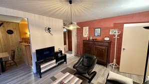 Un salón con televisor, un sillón de cuero negro, un mueble de madera y una pared roja.