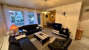 Una sala de estar con un sofá negro, una mesa de centro, un televisor y un mueble de madera.
