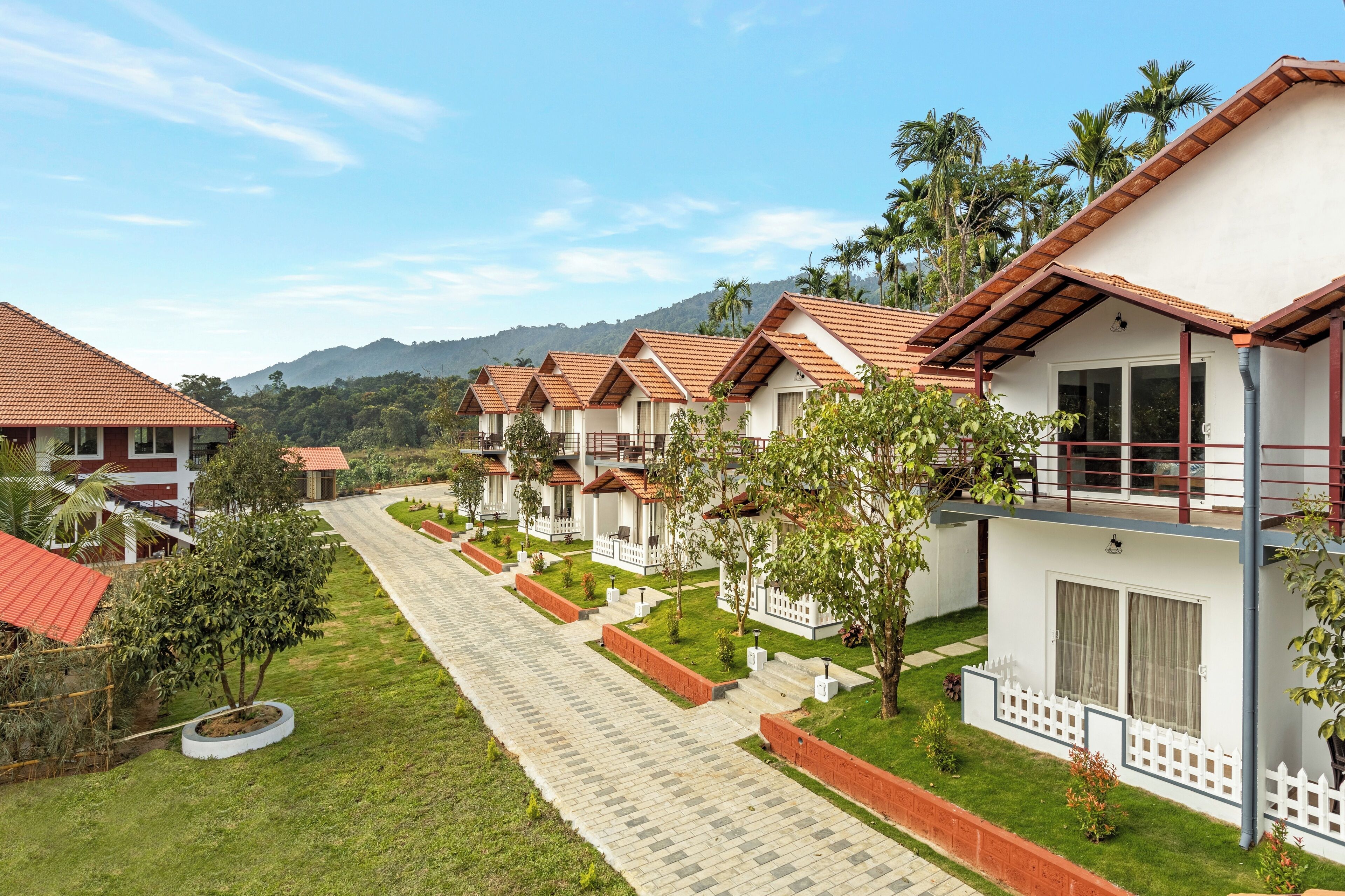 A row of bungalow-style accommodations with red-tiled roofs, white walls, and a paved pathway between them.