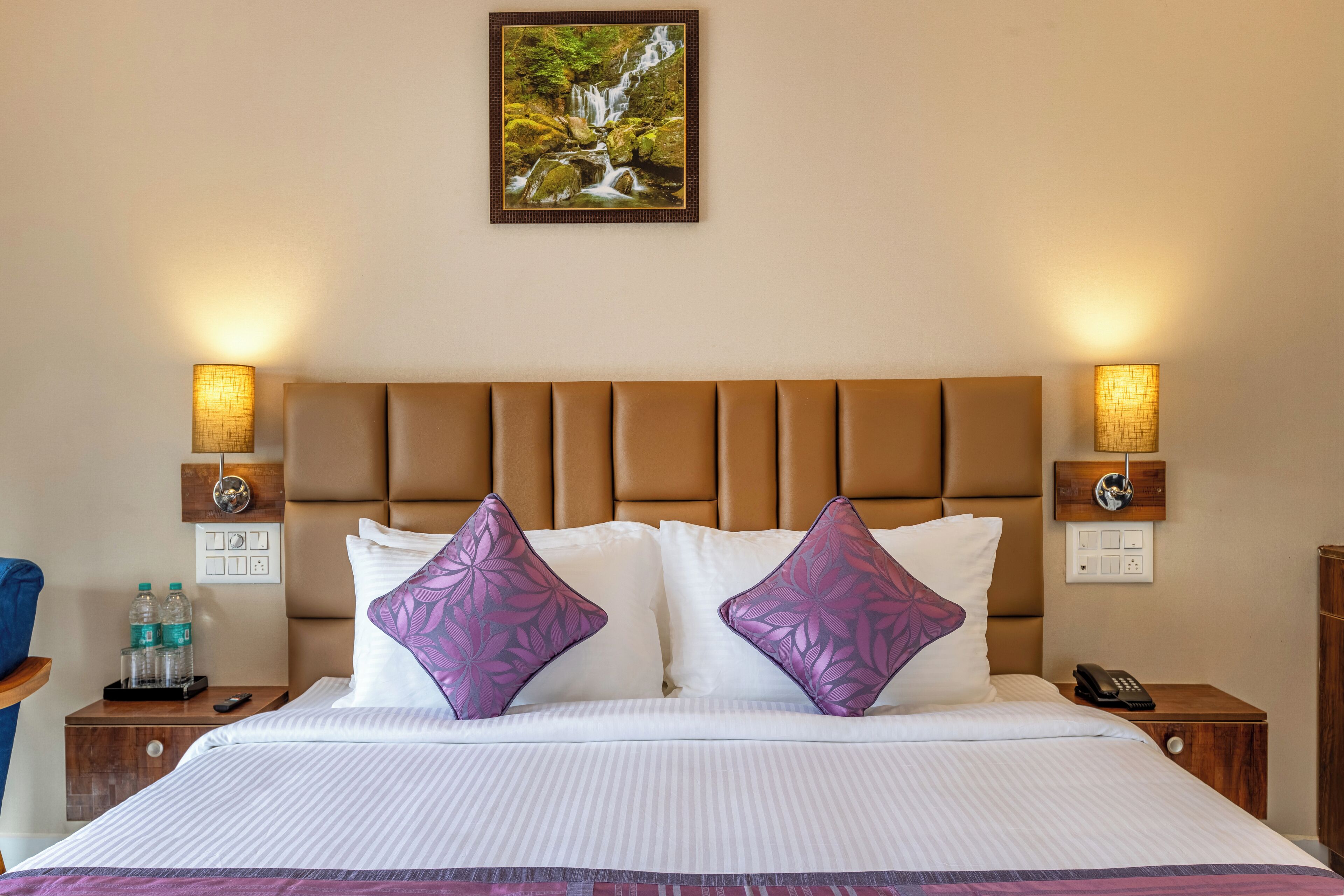 Een hotelkamer met een groot bed, twee nachtkastjes, een wandlamp en een lijst met een afbeelding van een waterval.