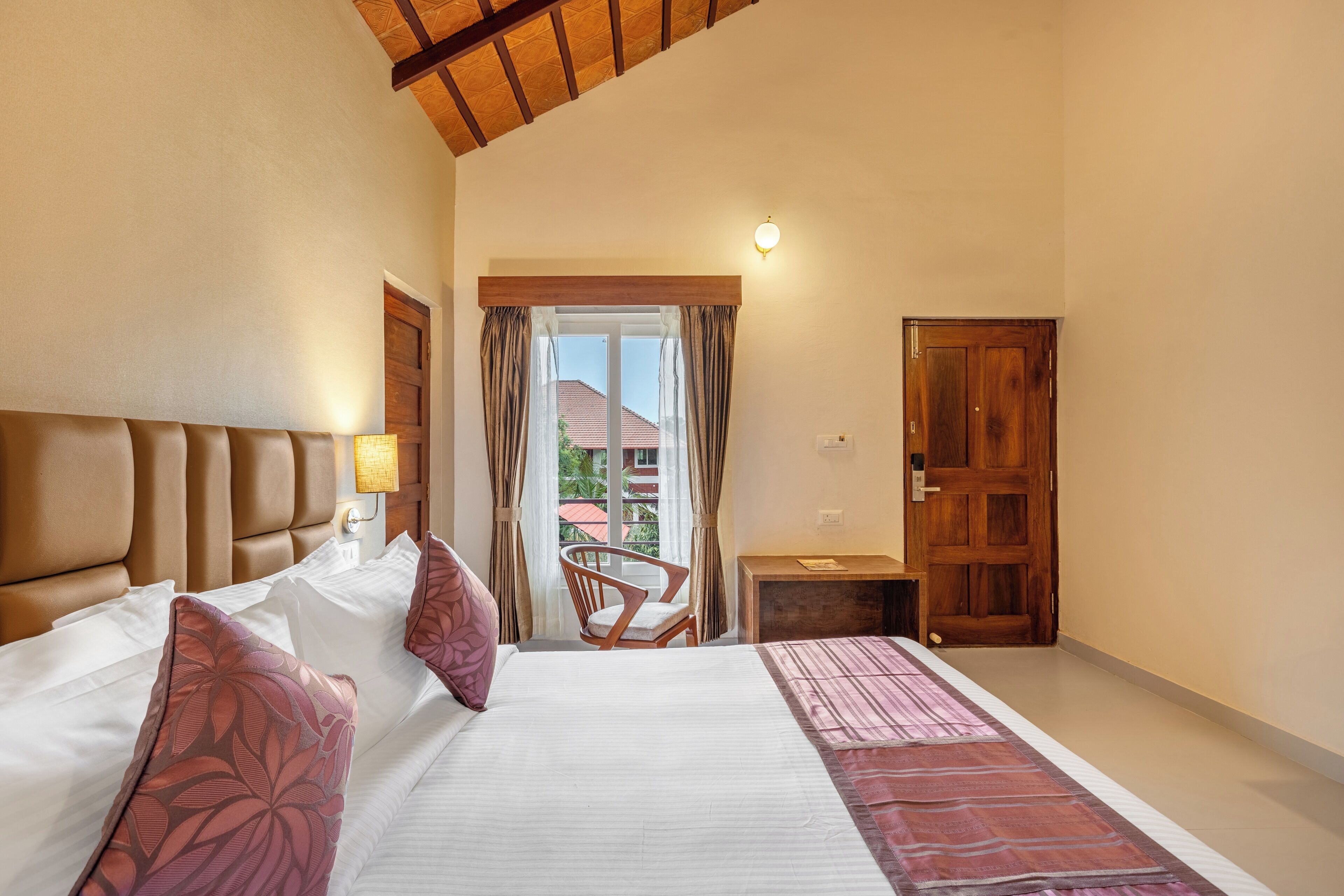 A hotel room with a large bed, a wooden headboard, a chair, a small table, and a view of the outside.
