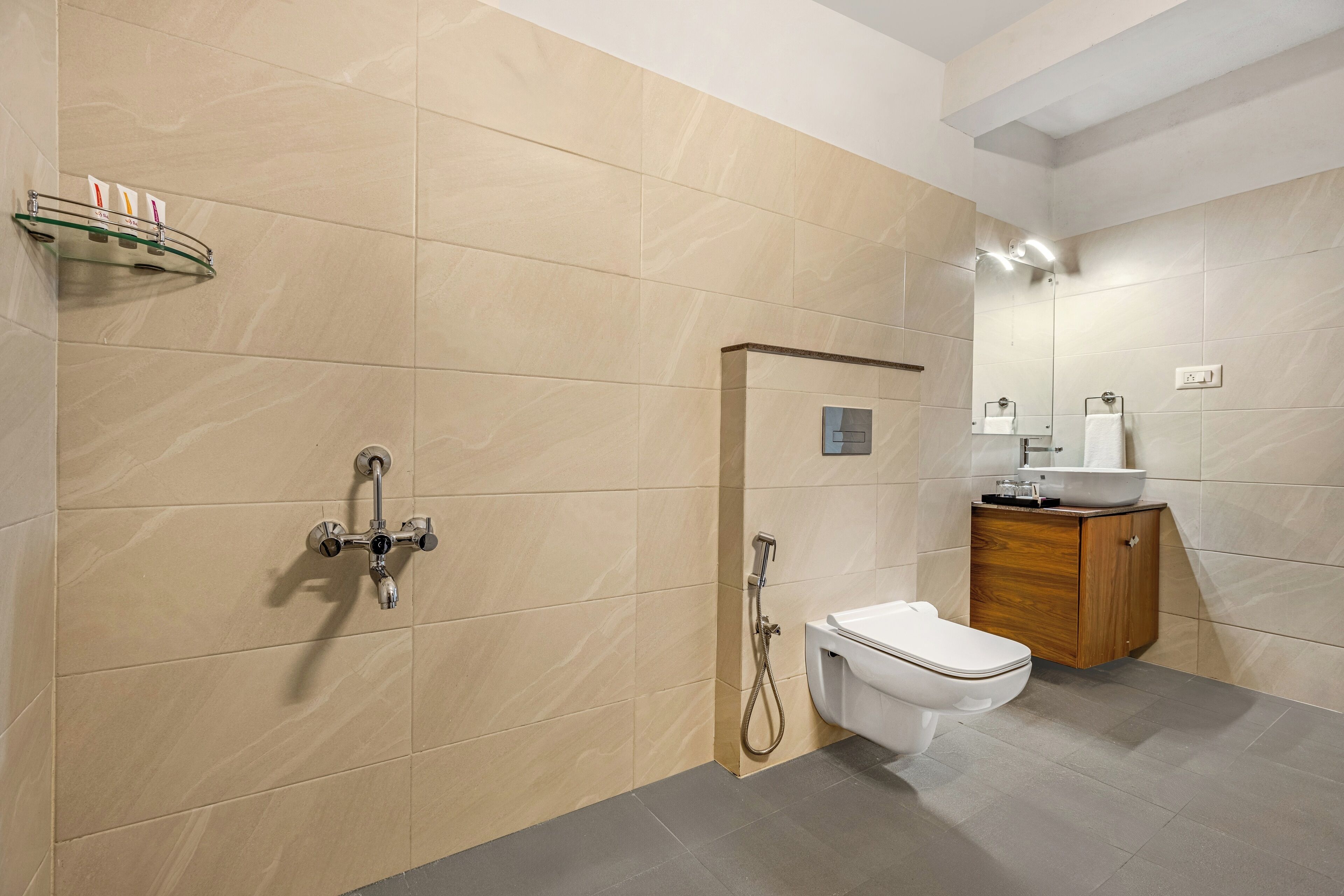 A modern bathroom with beige tiles, a glass shower enclosure, a white toilet, and a wooden vanity.