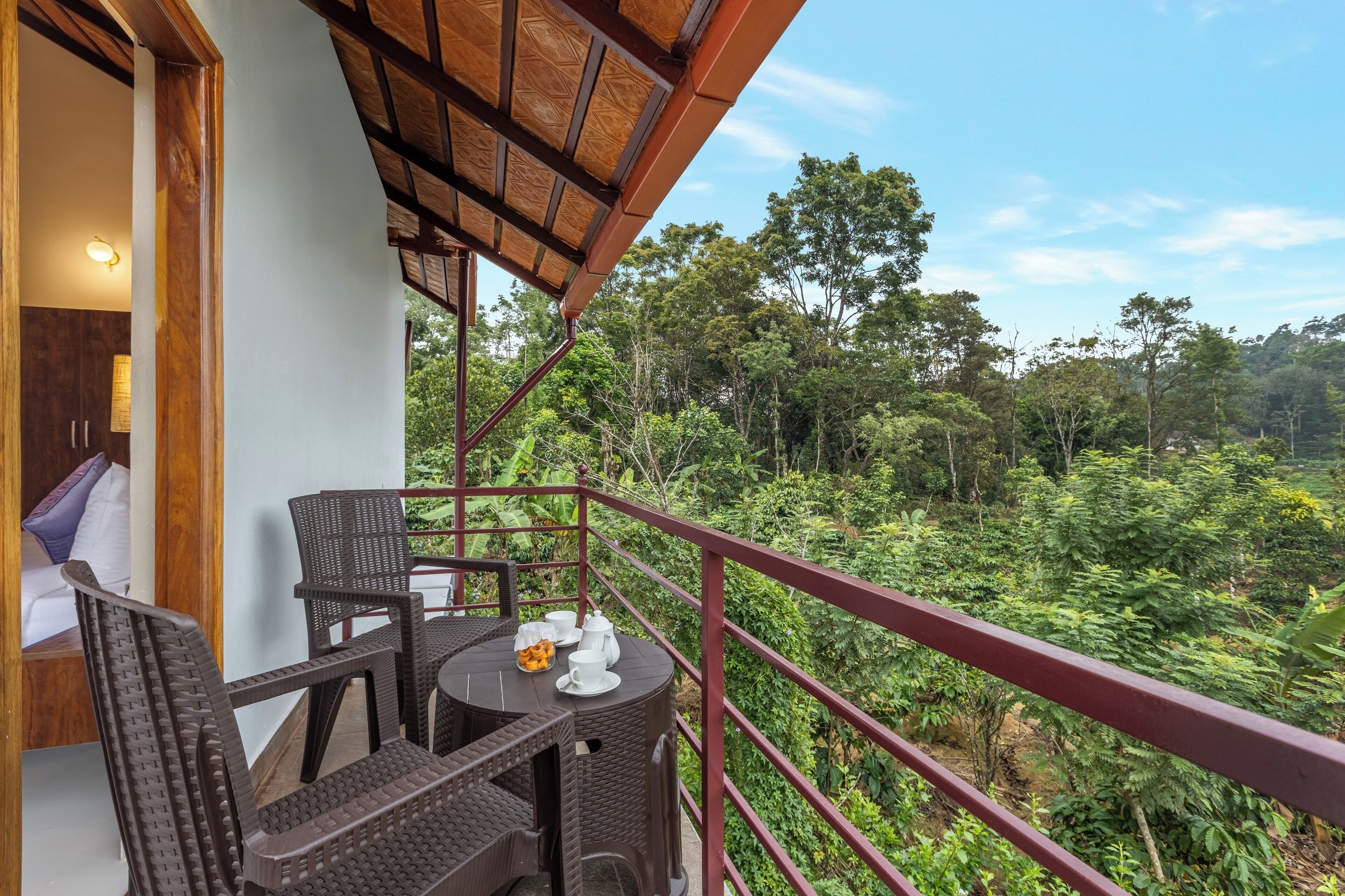A balcony with wicker furniture and a table set for tea, overlooking a lush forest.