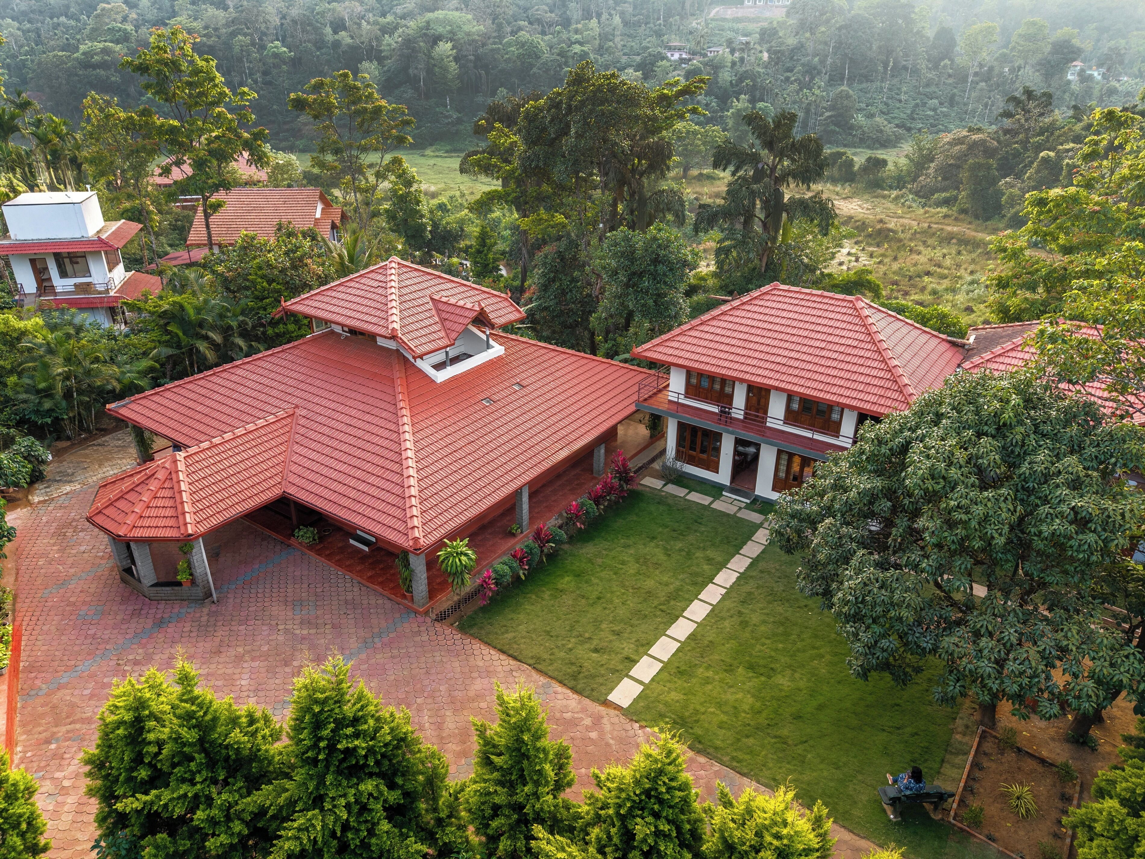 A large, two-story house with a red tiled roof, surrounded by lush greenery and a well-maintained lawn.
