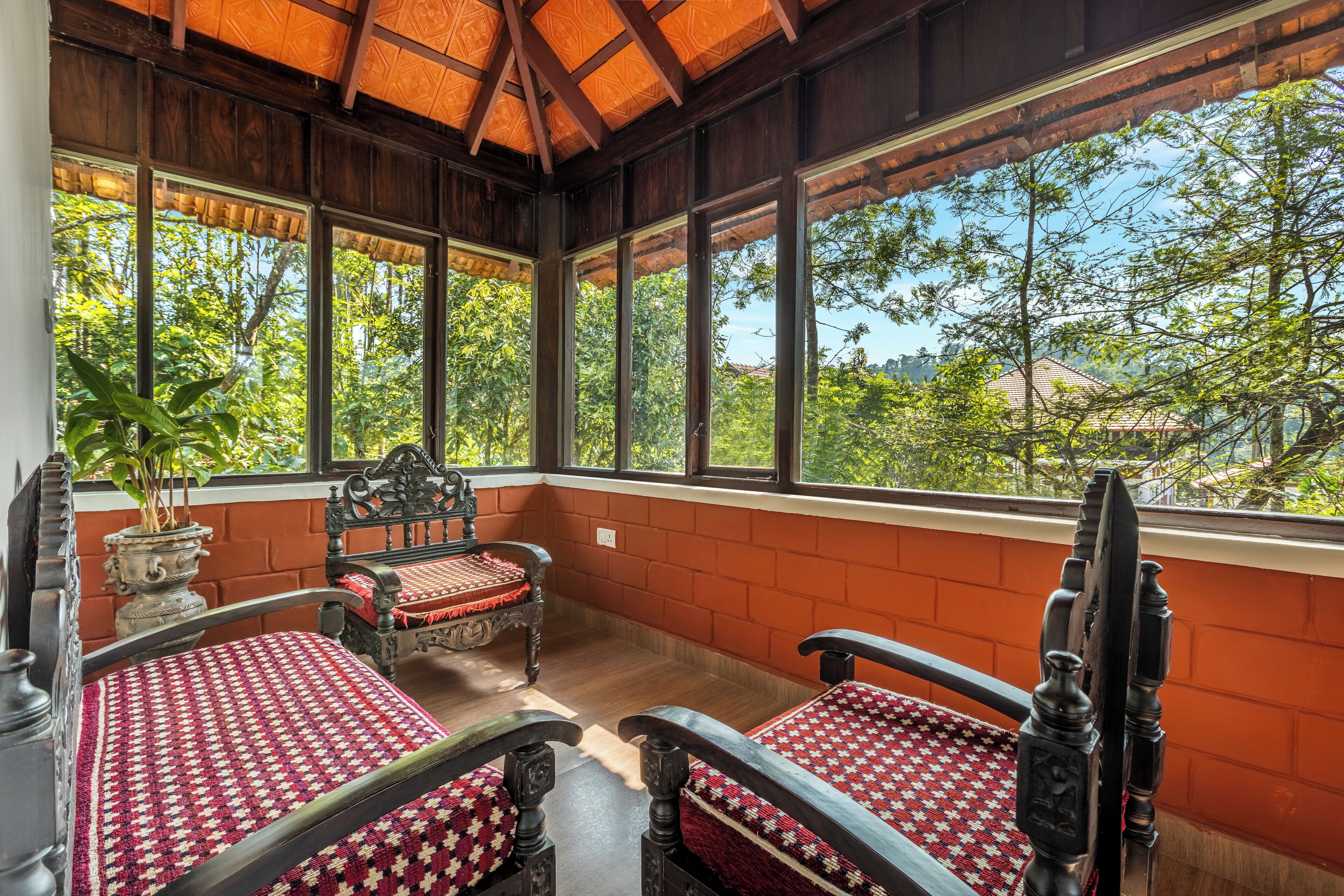 Una habitación con dos camas de madera, una planta en maceta y ventanas amplias que dan a vistas de árboles y edificios.