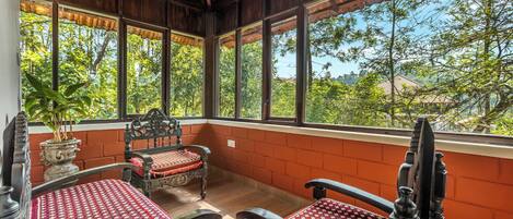 Una habitación con dos camas de madera, una planta en maceta y ventanas amplias que dan a vistas de árboles y edificios.