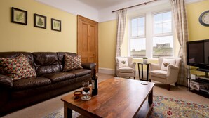 A living room with a brown leather sofa, a wooden coffee table, a beige armchair, and a television. - Old Duffus Farmhouse on Scottish Estate - stunning castle views (Elgin)