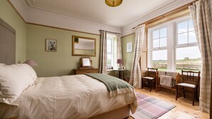 A bedroom with a large bed, a bedside table, a chair, a small table, a mirror, and a window with curtains. - Old Duffus Farmhouse on Scottish Estate - stunning castle views (Elgin)