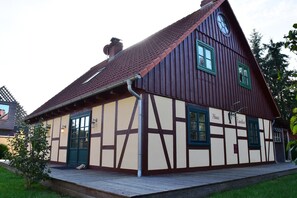 Ein traditionelles Fachwerkhäuschen mit steilem Satteldach, einem sichtbaren Schornstein und einer hölzernen Veranda.