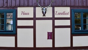 Eine Gebäudefassade mit zwei Schildern, auf denen 'Haus' und 'Landlust' stehen, oberhalb eines zentralen dekorativen Elements.