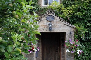 Een stenen cottage met een houten deur, een lantaarn boven de deur en een bordje met de tekst
