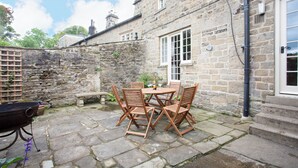 A stone building with a patio area featuring a table and chairs, a barbecue grill, and a stone wall. - Beautiful characterful cottage,family and dog friendly,quiet,close to amenities  (Harrogate)