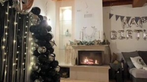 Ein gemütliches Wohnzimmer mit Holzbalkendecke, Kamin und einem 'HAPPY BIRTHDAY' Schriftzug.