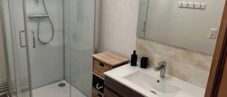 A modern bathroom with a glass-enclosed shower, a vanity with a mirror, and a tiled floor.