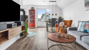 Ett modernt vardagsrum med en platt-TV, ett träinrett mediaskåp och en matplats med bord och stolar.