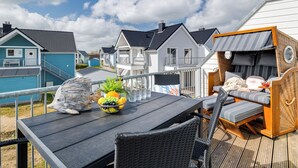 En terrass med ett bord dukat med frukt och glas, omgiven av flätade stolar och en bekväm sittgrupp med kuddar.