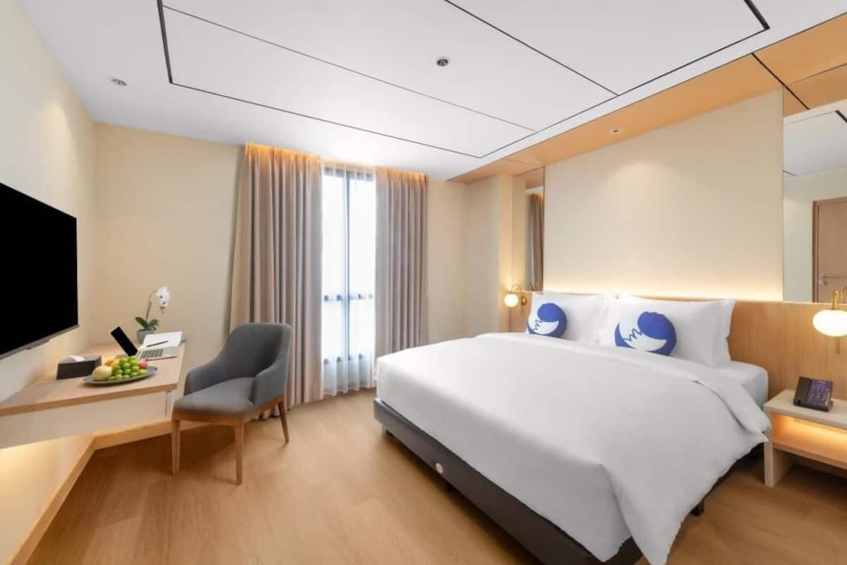 Ein modernes Hotelzimmer mit einem großen Bett, einem Schreibtisch mit einem Laptop, einem Sessel und einem Fernseher.