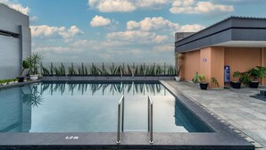 Una piscina con indicador de profundidad de 1,0 metro, rodeada de plantas en macetas y un edificio de madera con un letrero azul.